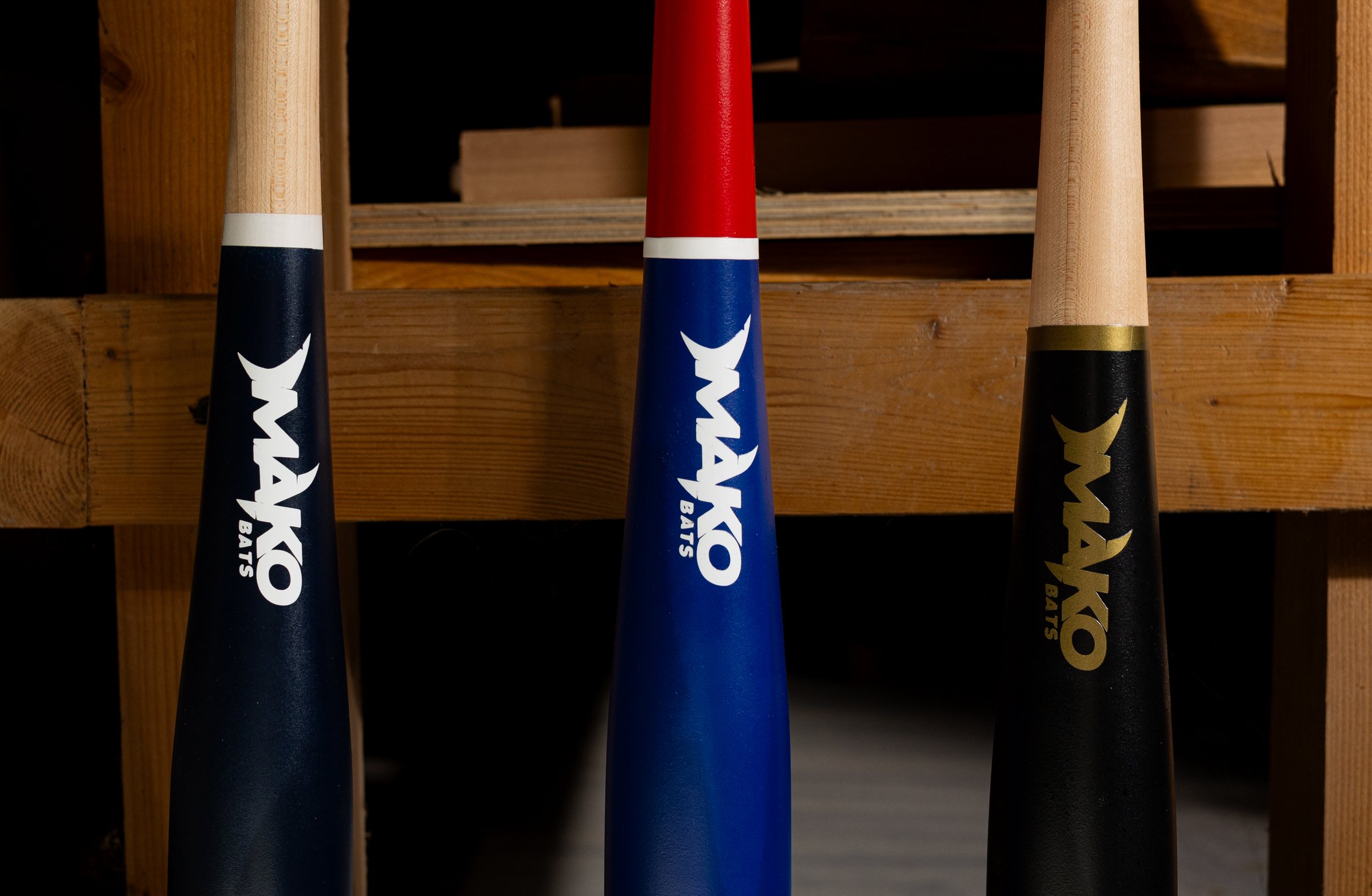 Three Mako bats racked in the shop: navy with a white ring, royal blue with a red handle, and black with a gold logo.